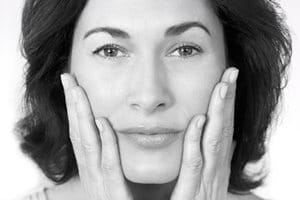 Жінка середнього віку обома руками торкається своїх щік.